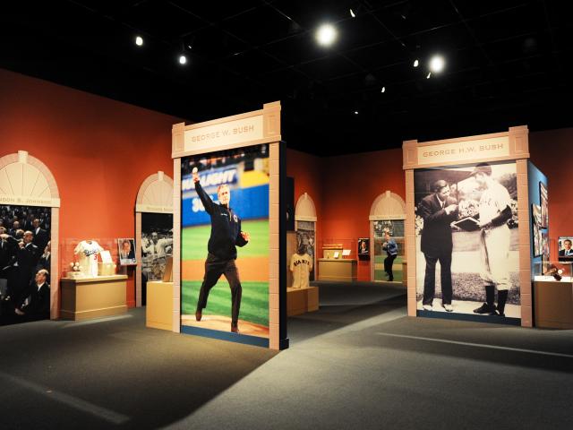 A photo of the 2015 exhibit 'Baseball: America's Presidents, America's Pastime,' at the George W Bush Library and Museum featuring a picture of President George W Bush throwing a first pitch