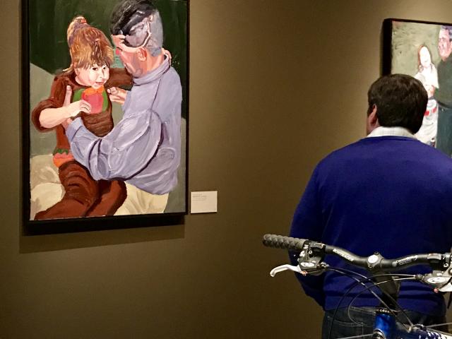 A photo of a visitor looking at a portrait of Scott Lilley and a young child, part of the 2017 exhibit Portraits of Courage, at the George W Bush Library and Museum