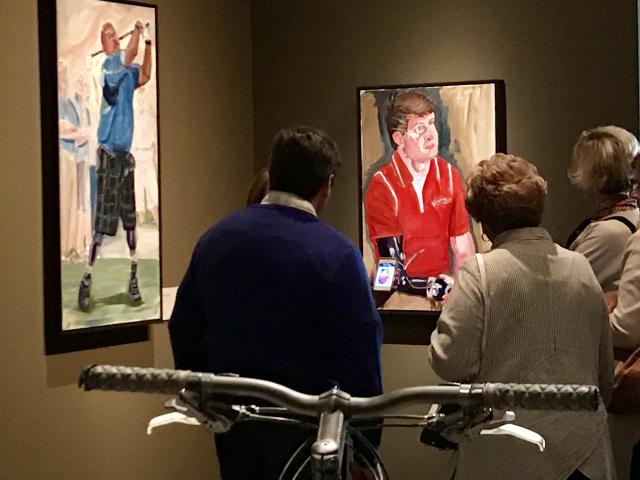 A photo of visitors looking at paintings of various athletes, from the 2017 exhibit Portraits of Courage, at the George W Bush Library and Museum 