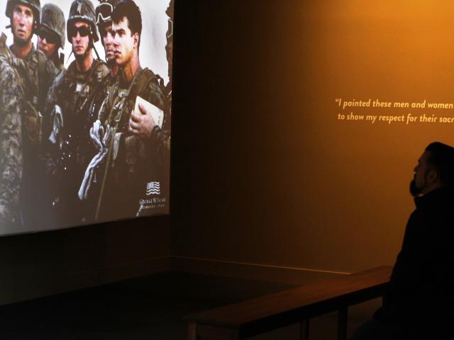 A photo of a visitors watching a short movie as part of the 2017 Portraits of Courage exhibit at the George W Bush Library and Museum.