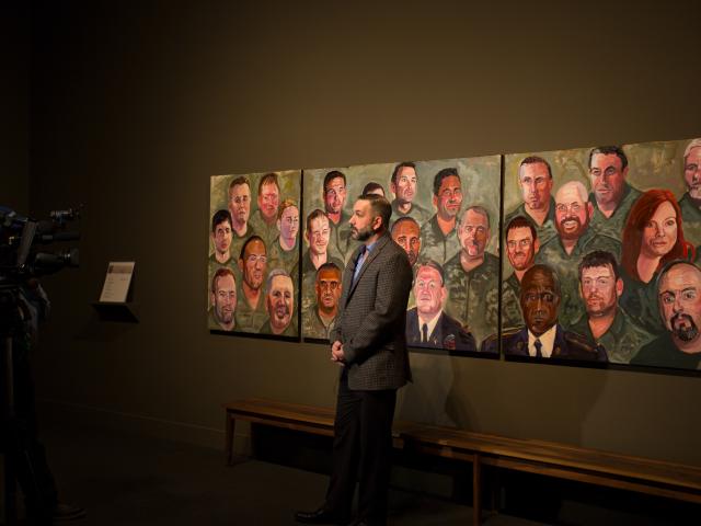 A photo of a man being interviewed while standing near his portrait panel, painted by President George W Bush, part of the 2017 exhibit Portraits of Courage, at the George W Bush Library and Museum