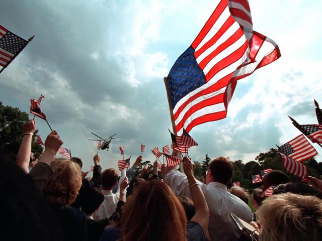 Crowd cheering and waving flags as helicopter flies away