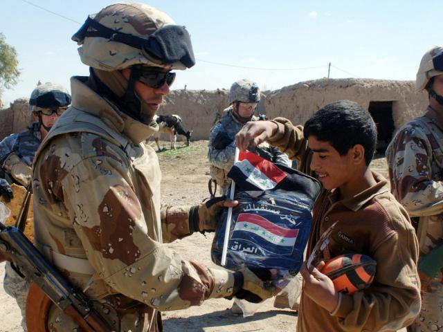 An Iraqi Army (IA) Soldier gives a local Iraqi boy a new Iraqi national flag and a new school backpack in 2006.