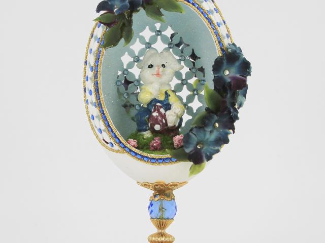 Green, white, and blue hand carved egg with an Easter bunny inside and affixed with rhinestones, miniature eggs, and flowers.